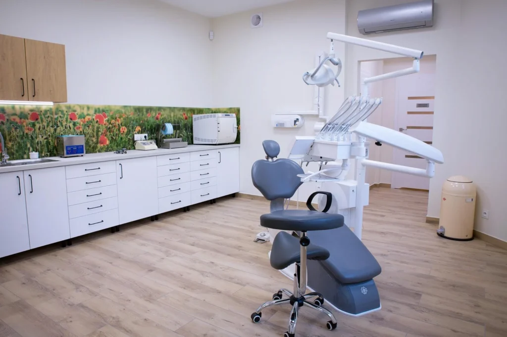 Wnętrze gabinetu stomatologicznego, z unitem, narzędziami. W tle szafki oraz tapeta w kwiaty.